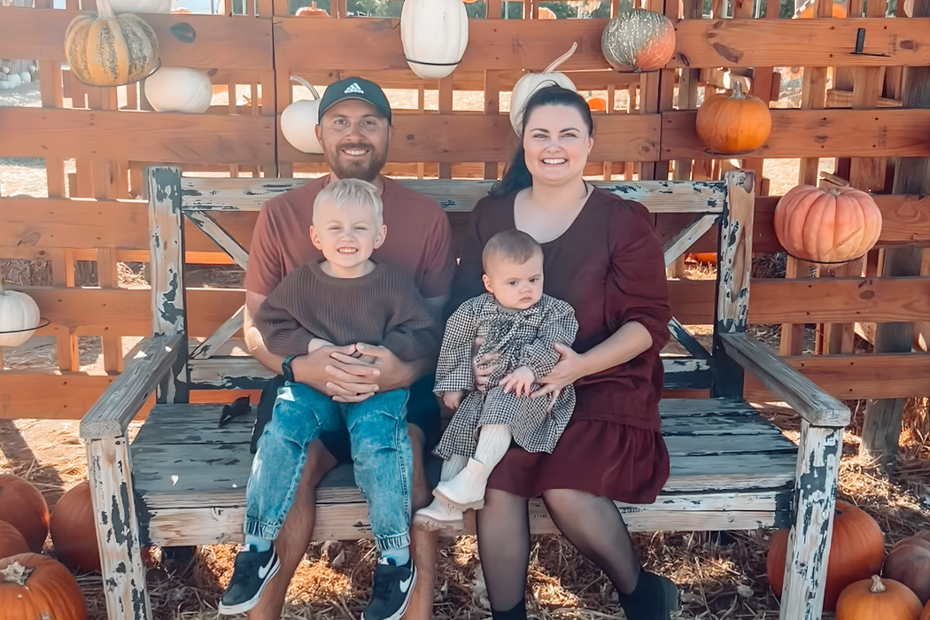 Family of four sitting on wooden bench with pumpkins in outdoor fall setting